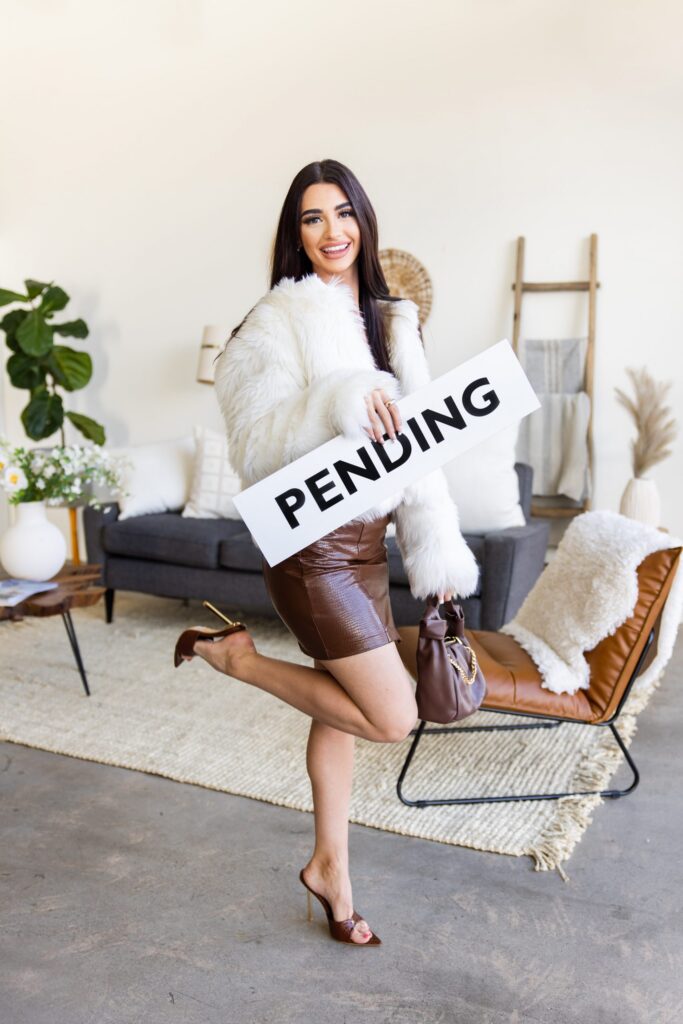 Smiling real estate agent holding a pending sign in a modern staged home in boise idaho.