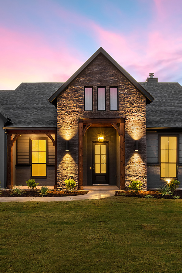 Inviting modern farmhouse with stone entryway and warm evening lighting, showcasing strong curb appeal in Boise Idaho.